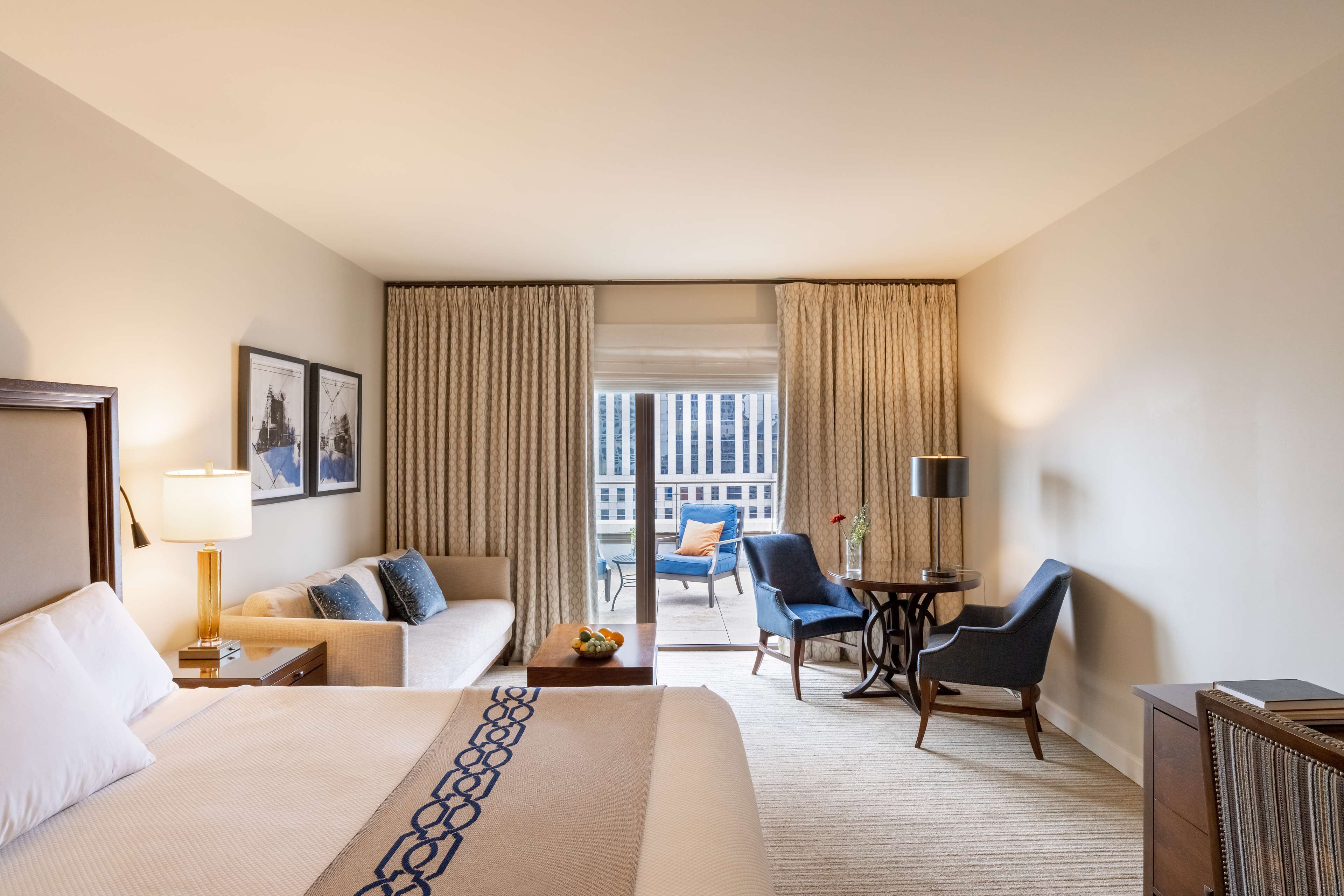 Een hotelkamer met een groot bed, een slaapbank, een bureau met lamp, een stoel en een balkon met uitzicht op gebouwen.