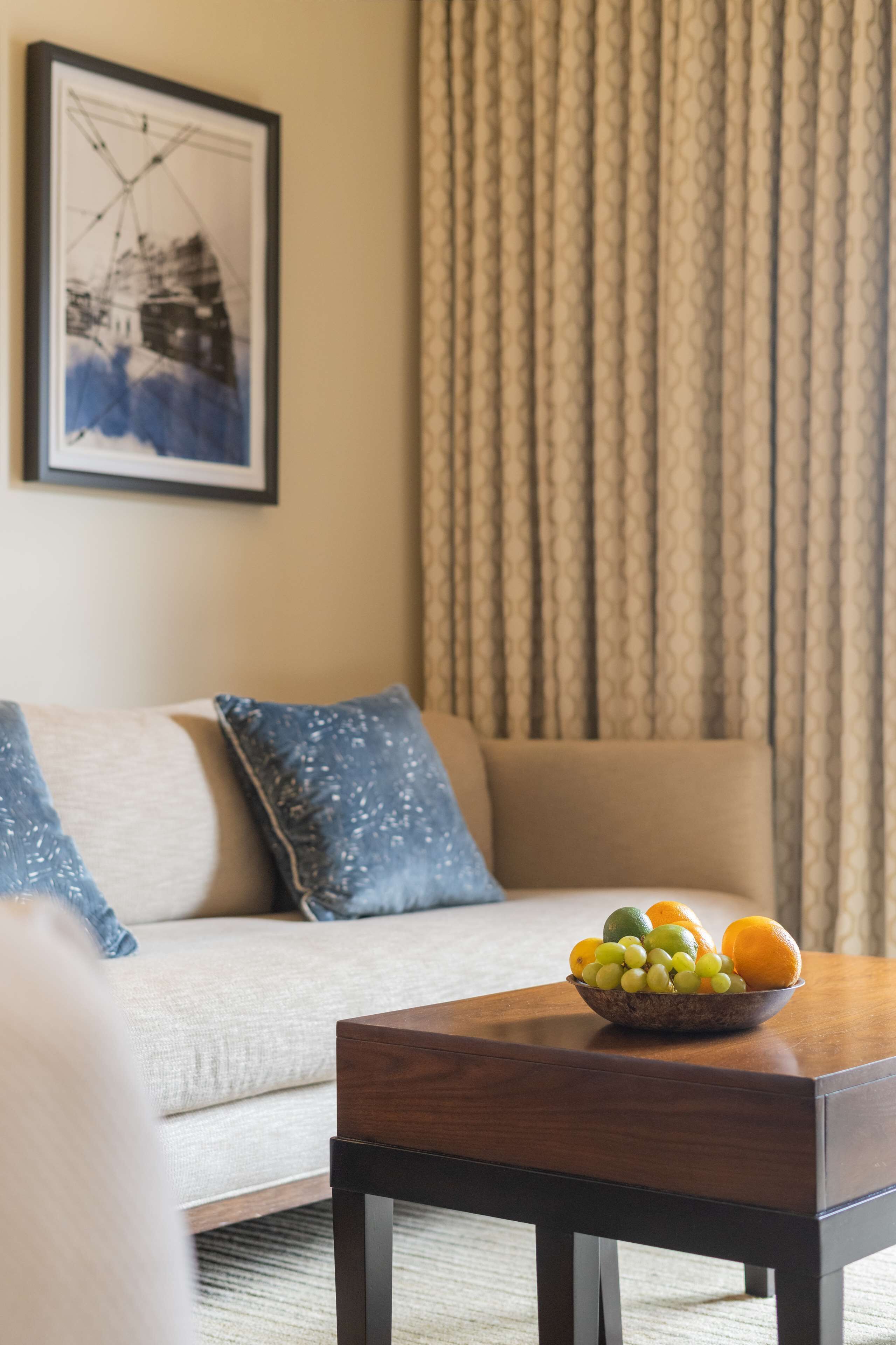 Una sala de estar con sofá, una mesa de centro con un frutero y una cortina estampada.