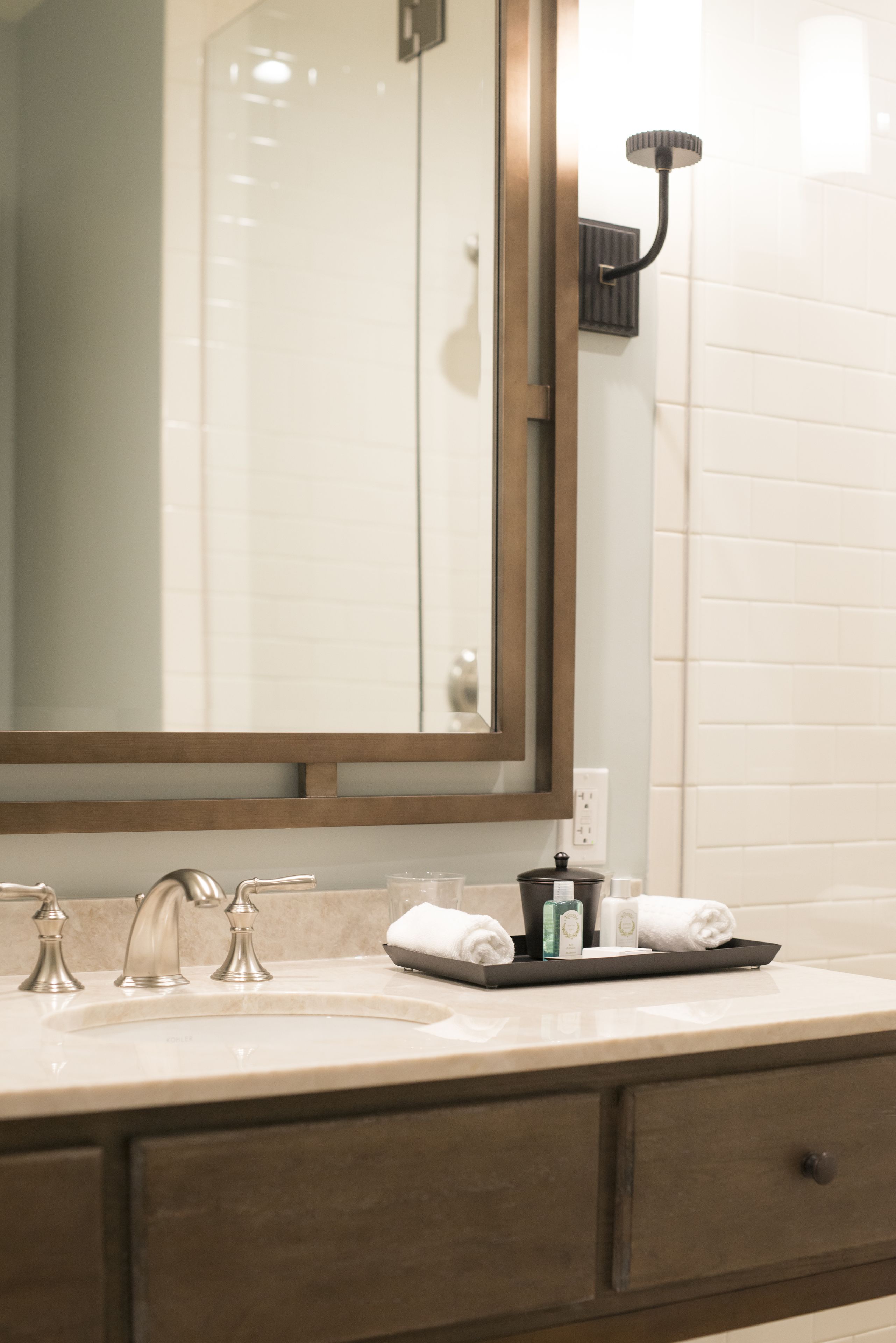 A bathroom with a large mirror, a sink with two faucets, and a towel rack.