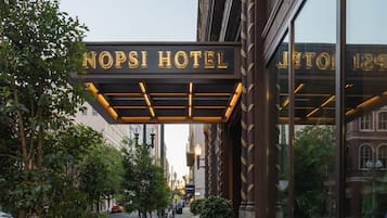 The NOPSI HOTEL entrance with a covered walkway, potted plants, and a clear view of the street.