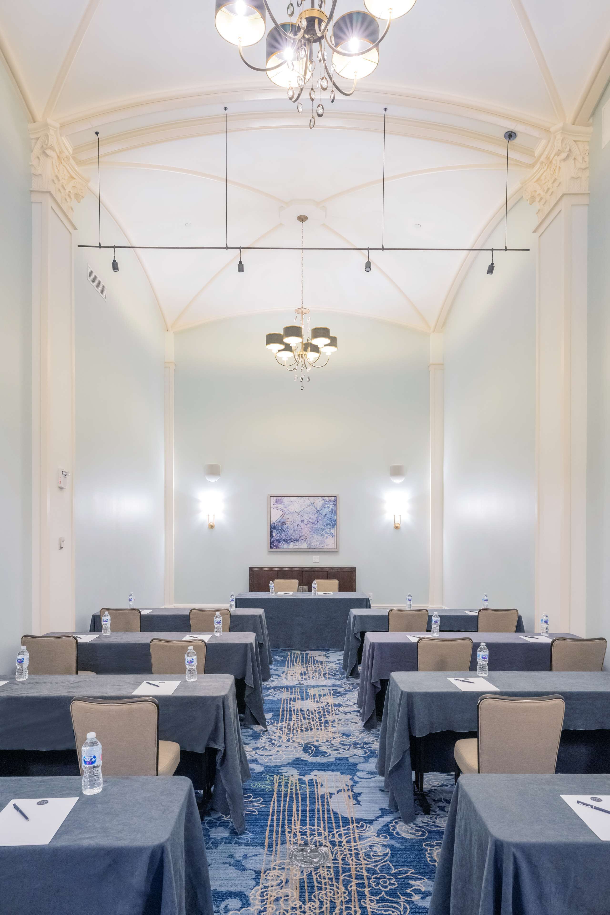 Una sala conferenze con tavoli, sedie, un lampadario e un tappeto blu.