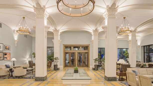 A spacious lobby with high ceilings, large chandeliers, and a central glass table.