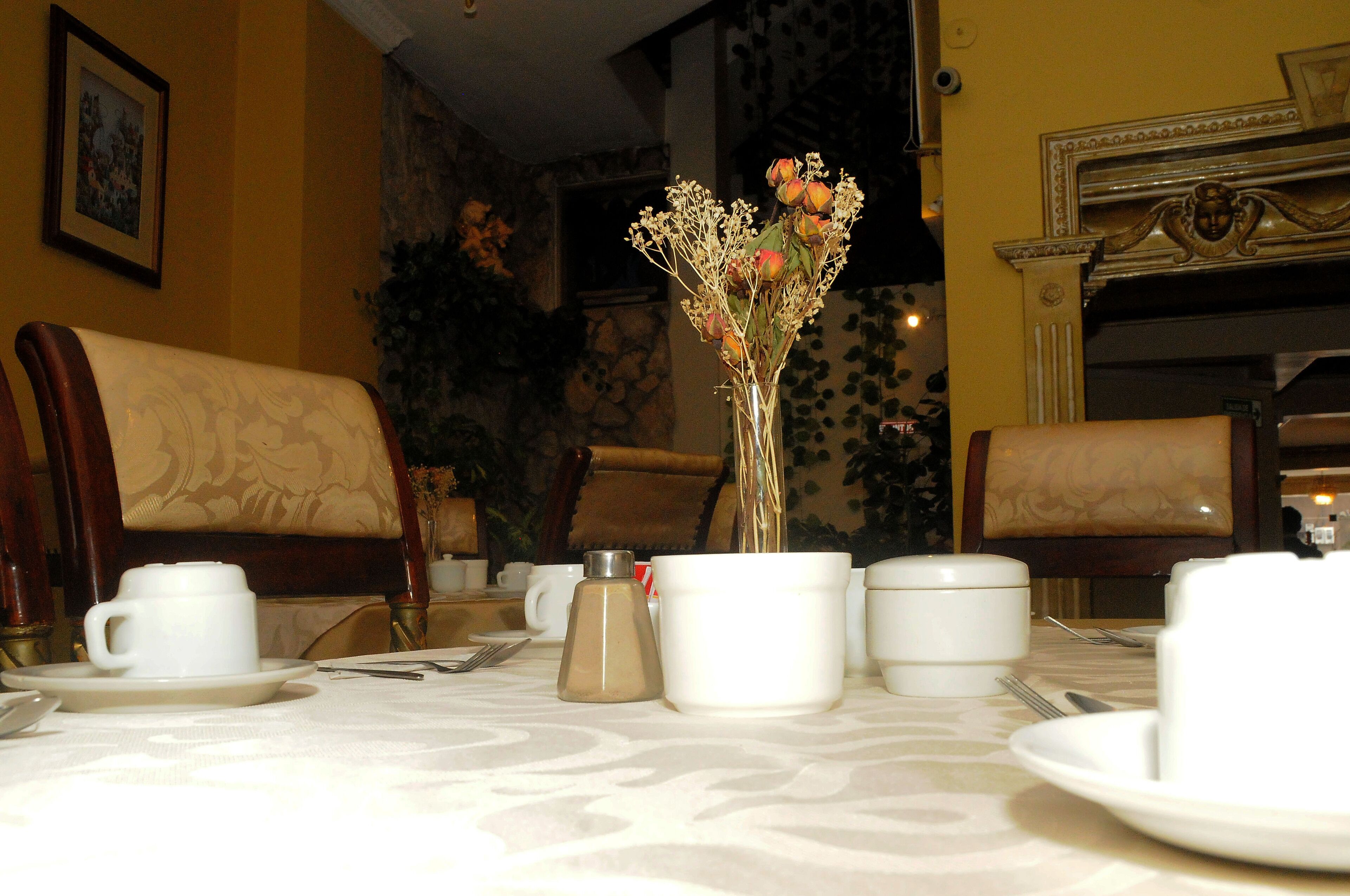 A dining table set with white cups, saucers, and a silver condiment bottle.