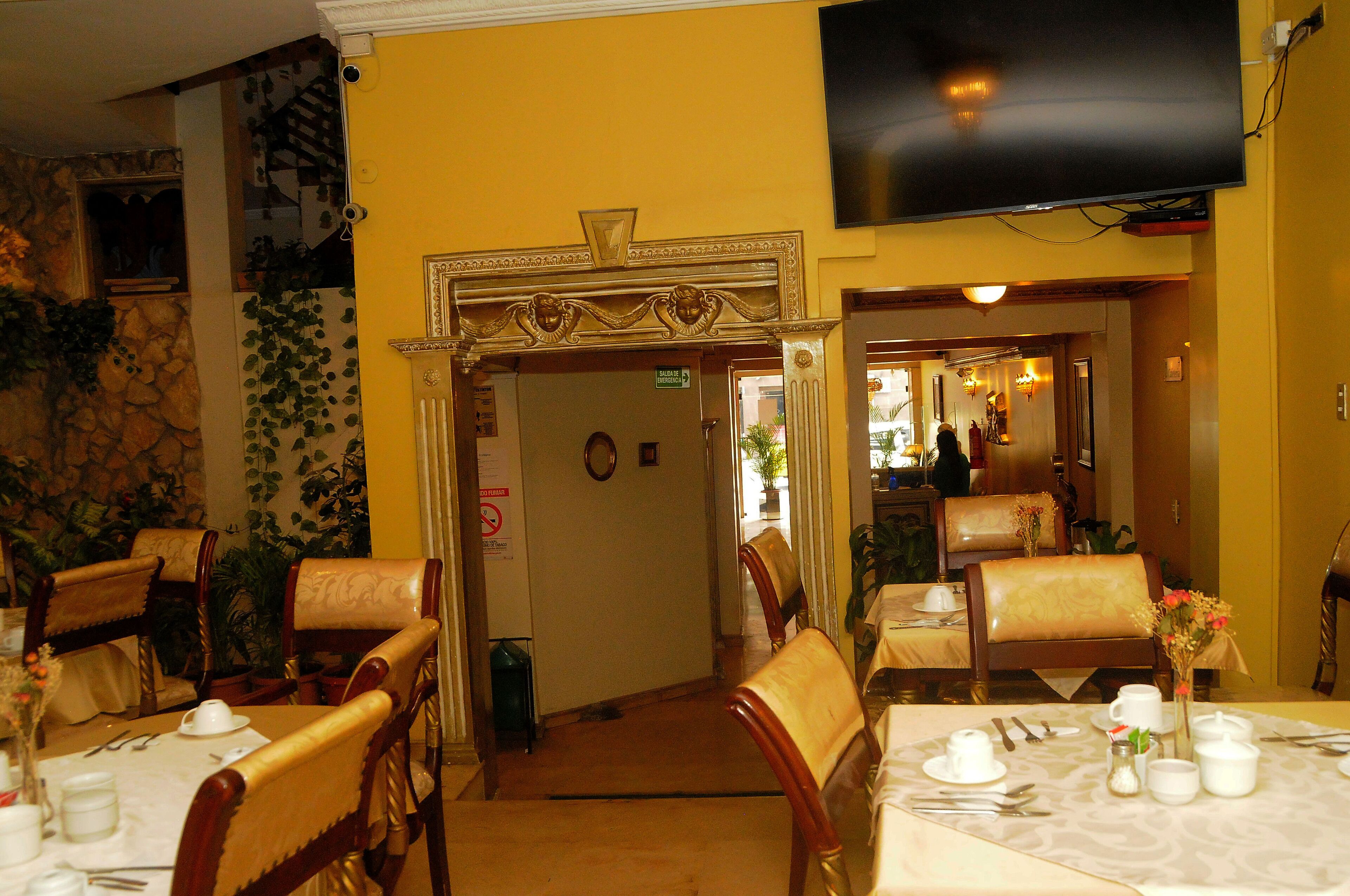 Un comedor con mesas dispuestas para el servicio, sillas y un televisor montado en la pared.