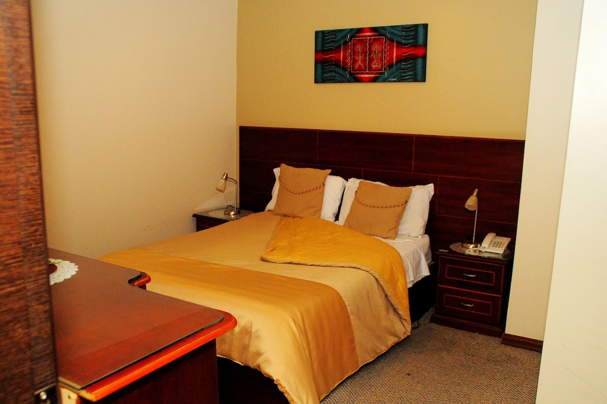 Habitación de hotel con cama, mesita de noche, escritorio y un cuadro en la pared.