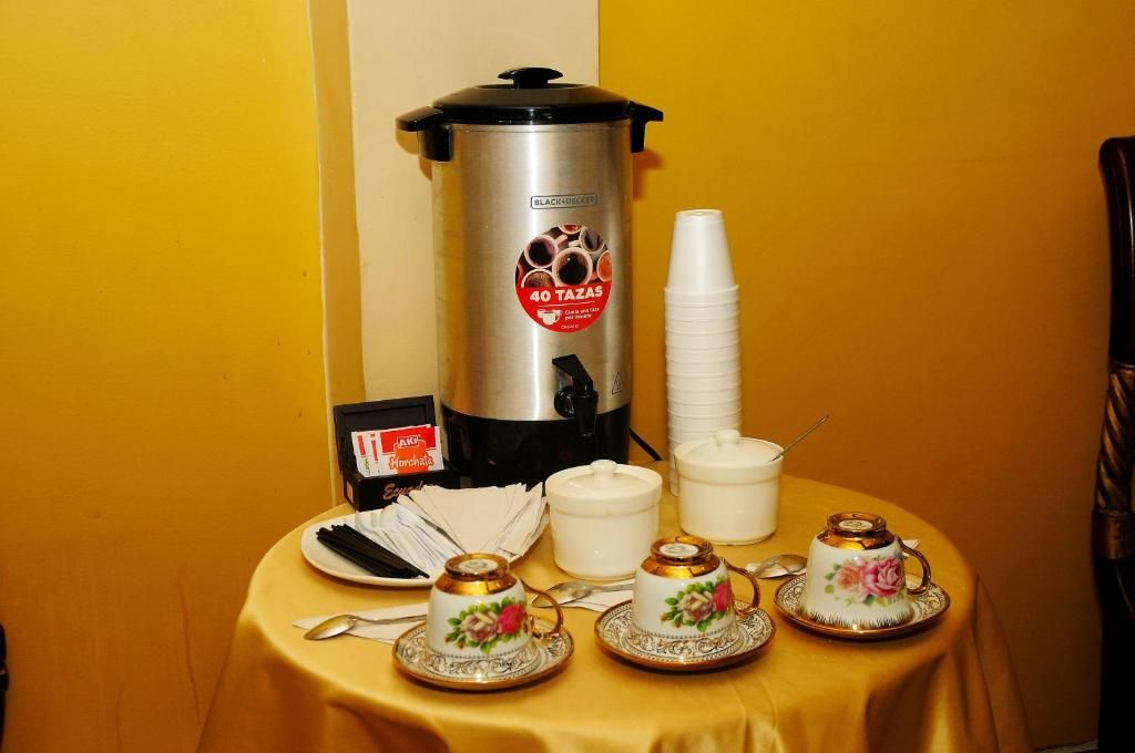 A coffee station with a coffee maker, disposable cups, and teacups on a table.