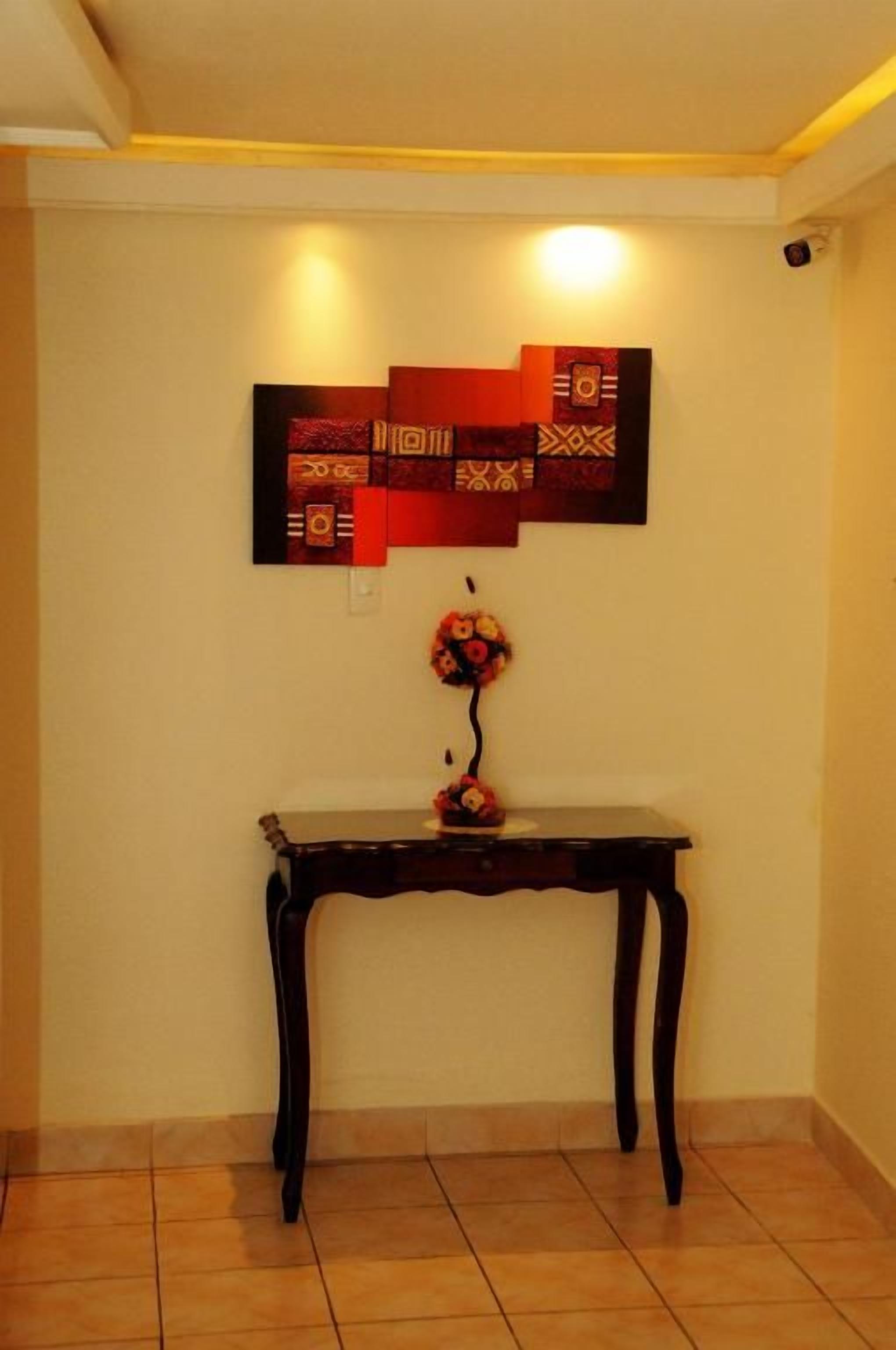 Een kamer met een donker houten console tafel tegen een muur, een decoratieve wanddecoratie erboven, en een kleine vaas met bloemen op de tafel.