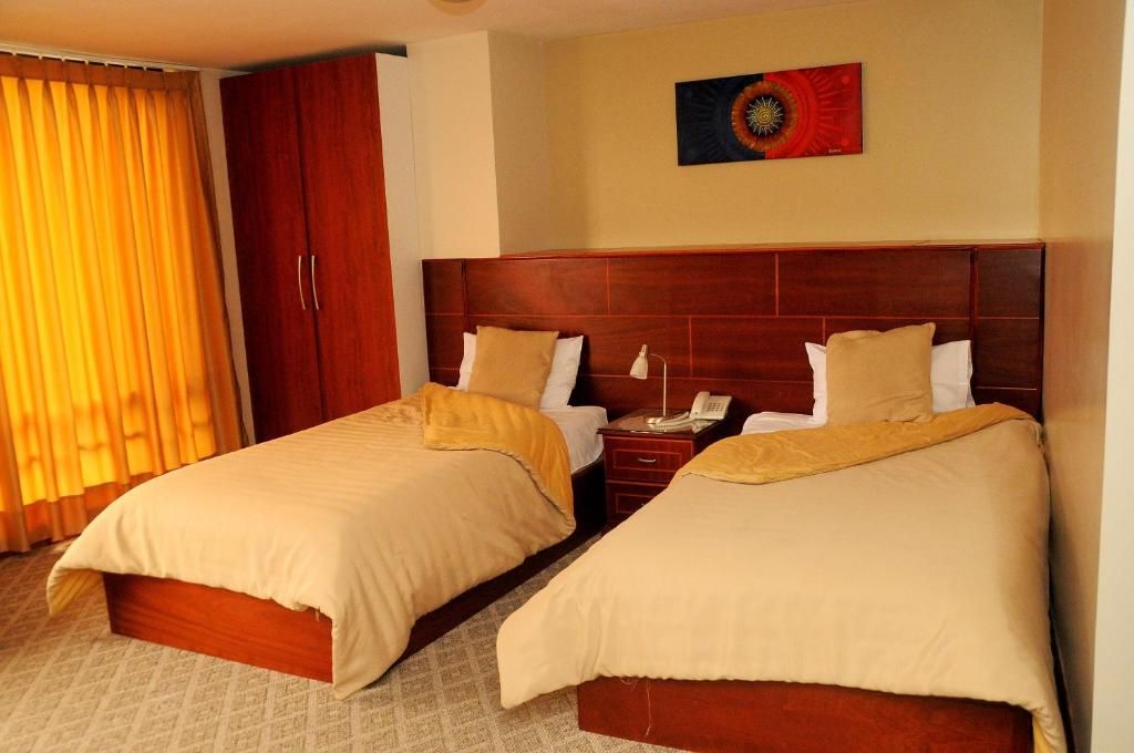 Habitación de hotel con dos camas, cabecero de madera, teléfono y un cuadro en la pared.