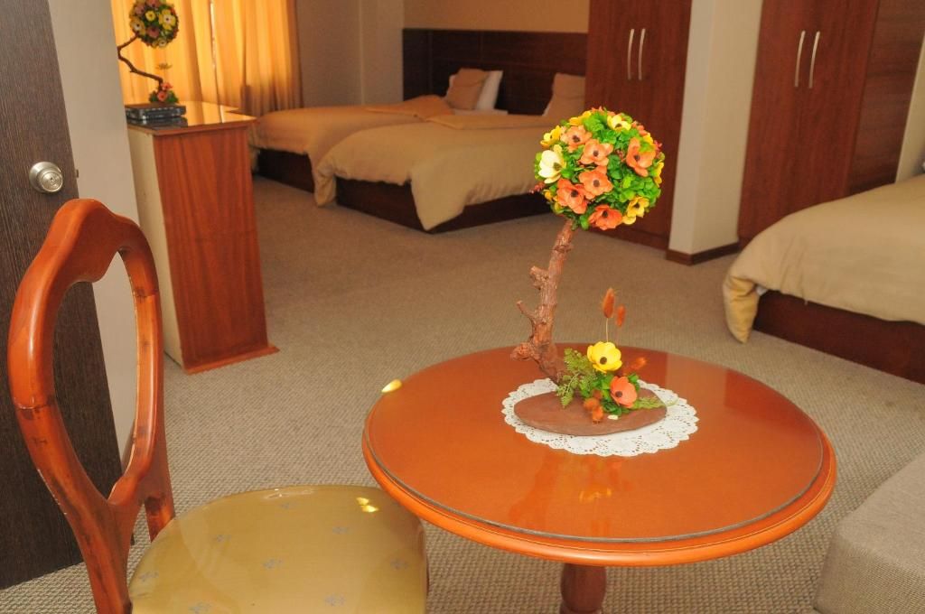 A hotel room with a bed, a small round table with a vase of flowers, a chair, and a wardrobe.