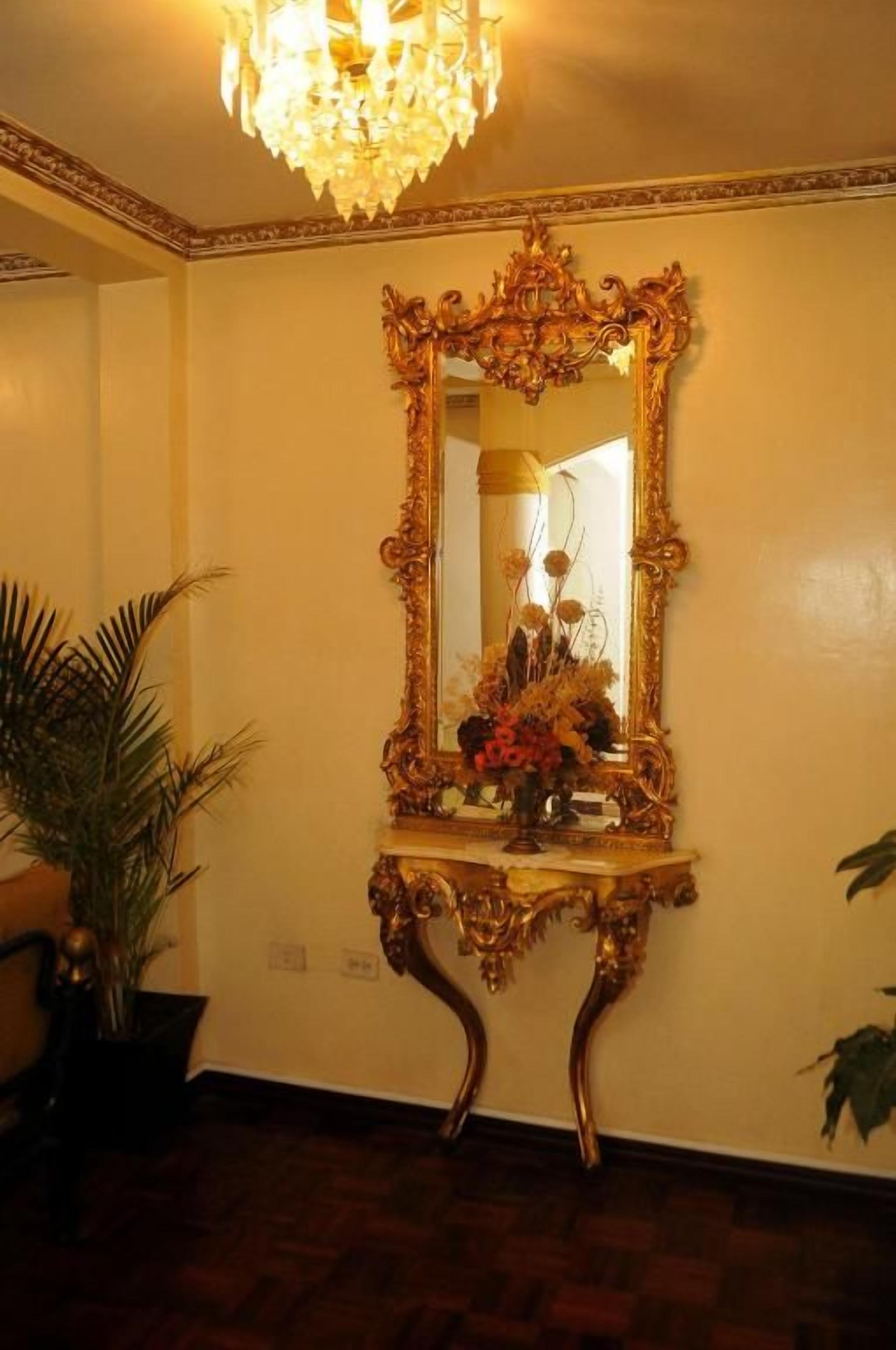 Una habitación con un espejo grande y ornamentado sobre un aparador, un candelabro y plantas en macetas.