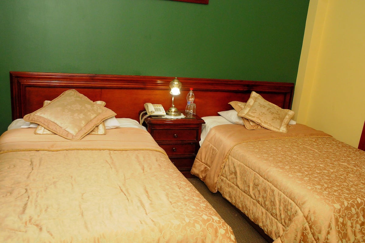 Una cama doble con cabecera de madera, una mesita de noche con lámpara y un teléfono.