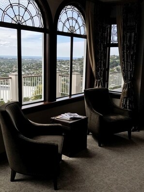 A room with two leather armchairs, a small table with magazines, and large windows with a view of a residential area.