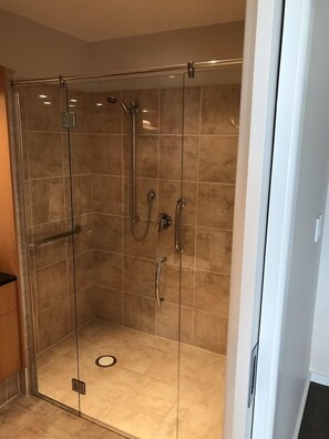 A glass-enclosed shower with multiple fixtures, including a handheld showerhead, a wall-mounted faucet, and a handheld showerhead.