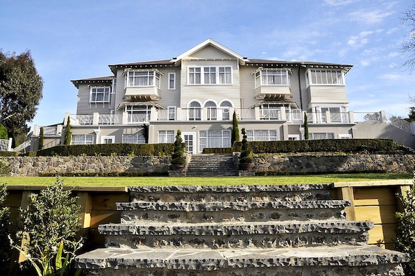 A large, two-story building with a symmetrical facade, multiple windows, and a stone staircase leading to the entrance.