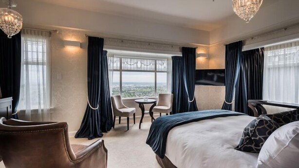 A hotel room with a large bed, two armchairs, a small table, and a TV. - Hackthorne Gardens Luxury Accommodation (Christchurch)