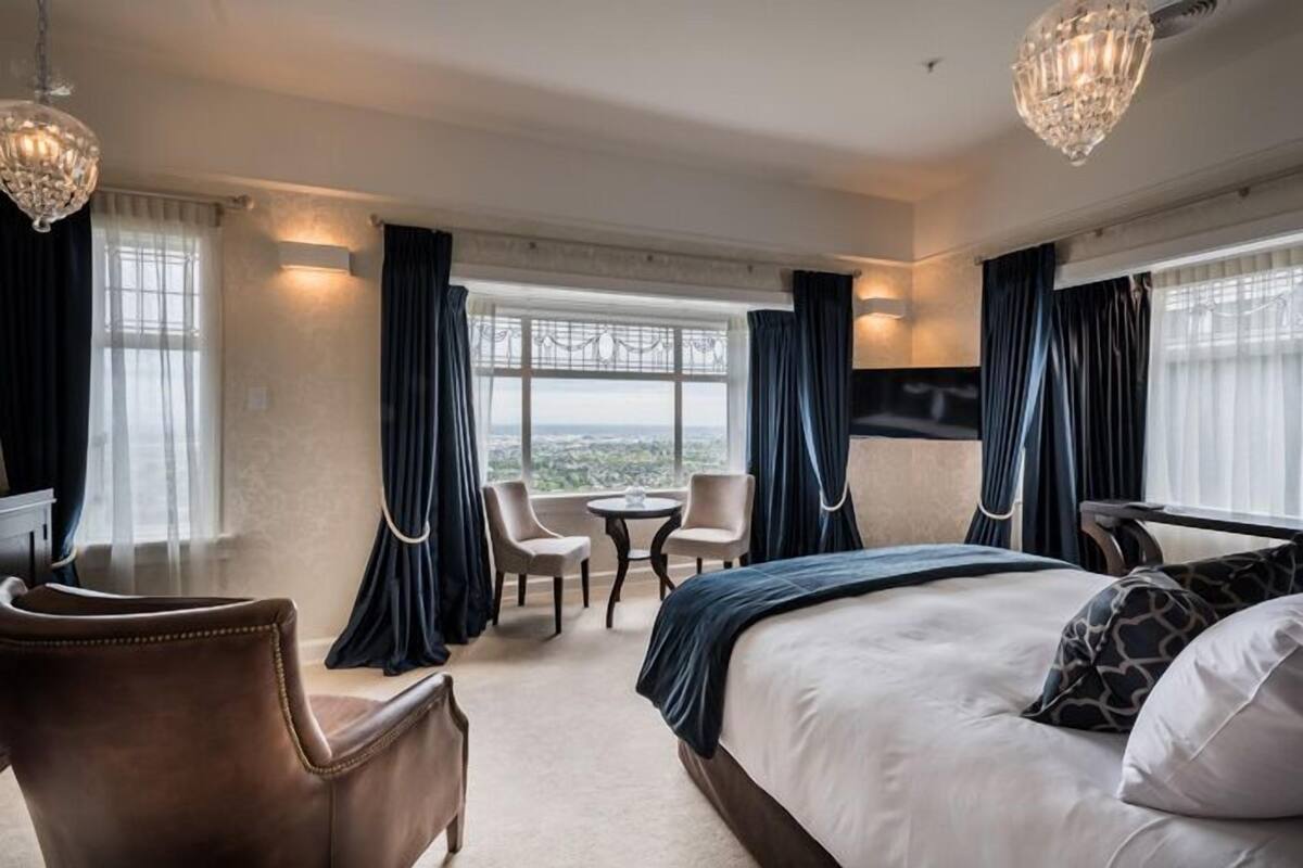 A hotel room with a large bed, two armchairs, a small table, and a TV.