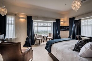 Une chambre d’hôtel avec un grand lit, deux fauteuils, une petite table et un téléviseur.