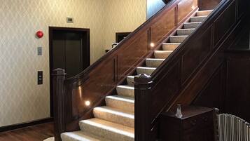 A curved wooden staircase with a carpeted landing and a handrail, leading to an elevator.