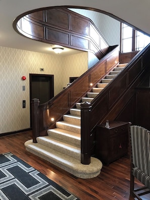 A curved wooden staircase with a carpeted landing and a handrail, leading to an elevator.