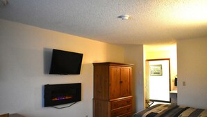 A bedroom with a TV mounted on the wall, a wooden cabinet, and a bed with a striped blanket. - Country Inn (Libby)