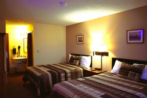 A hotel room with two beds, a bedside table with a lamp, a small desk with a telephone, and a picture on the wall.