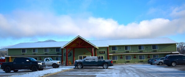 A motel with a large entrance, multiple rooms, and a parking area with several vehicles.