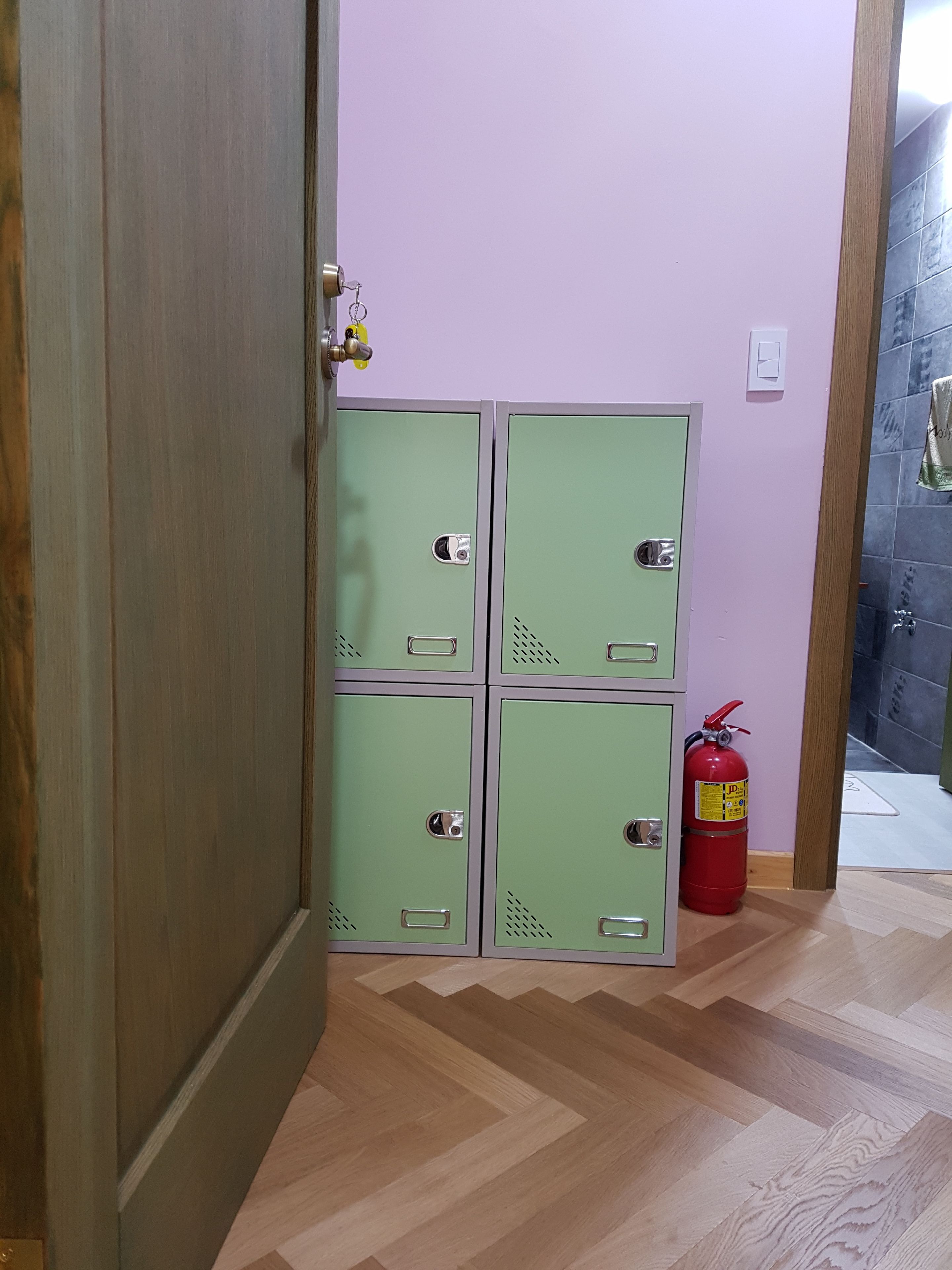 A room with four green lockers, a fire extinguisher, and a wooden door.