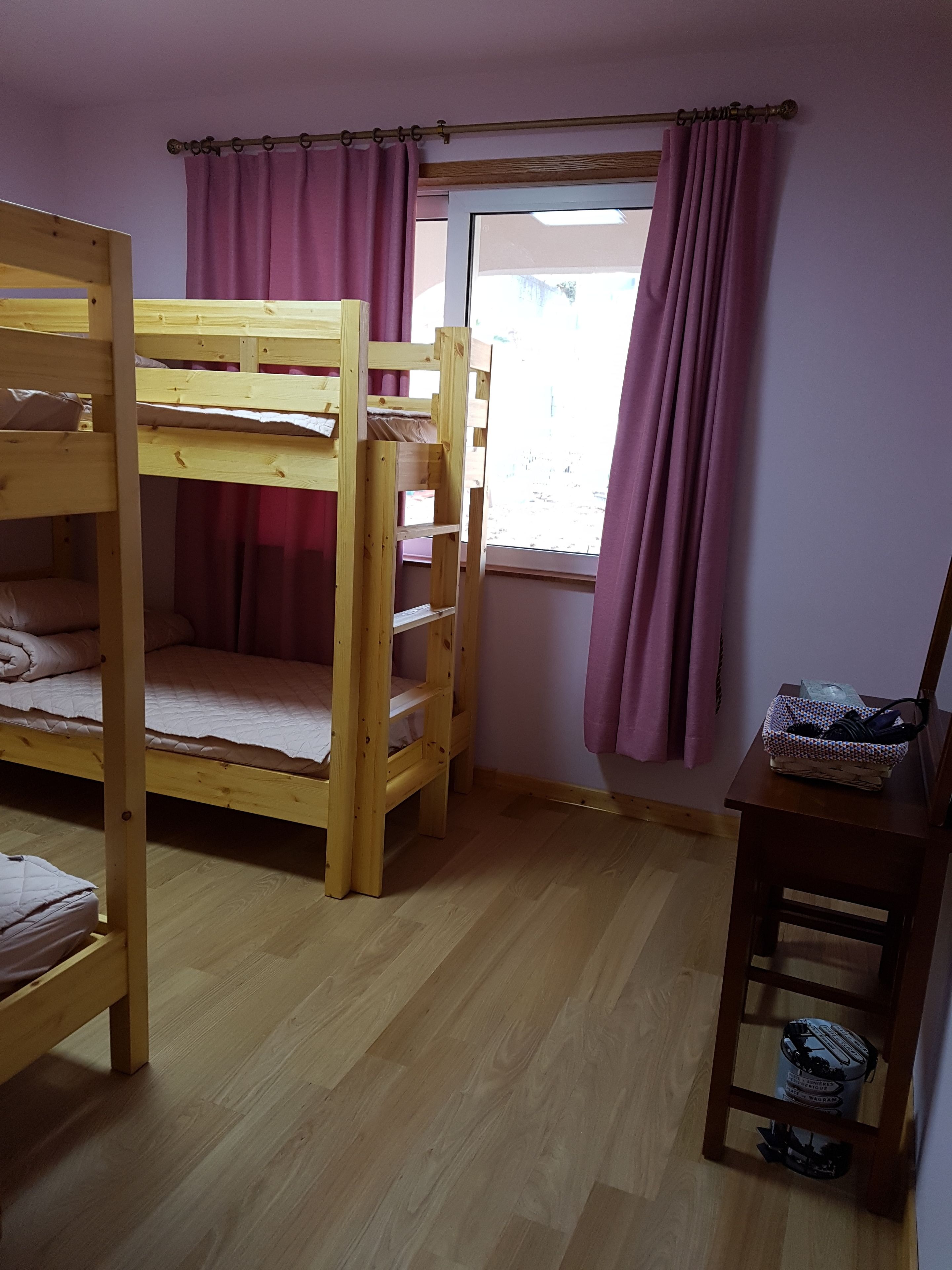 Una habitación con dos literas, una ventana con cortinas, un escritorio de madera y una cesta sobre el escritorio.