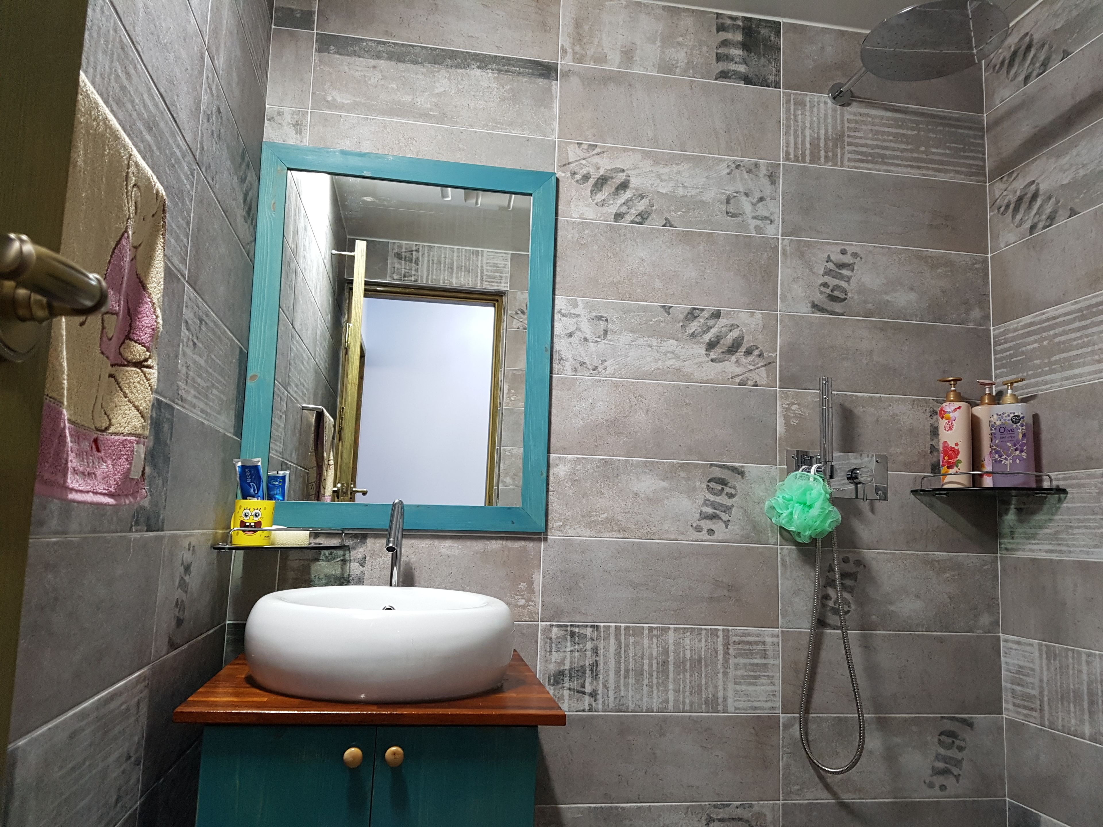 Un baño con un lavabo blanco, un mueble color esmeralda, un espejo con marco azul y paredes con azulejos.