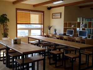 Une bibliothèque avec des tables et des chaises en bois, une grande fenêtre avec des stores et plusieurs écrans d’ordinateur placés sur des étagères.