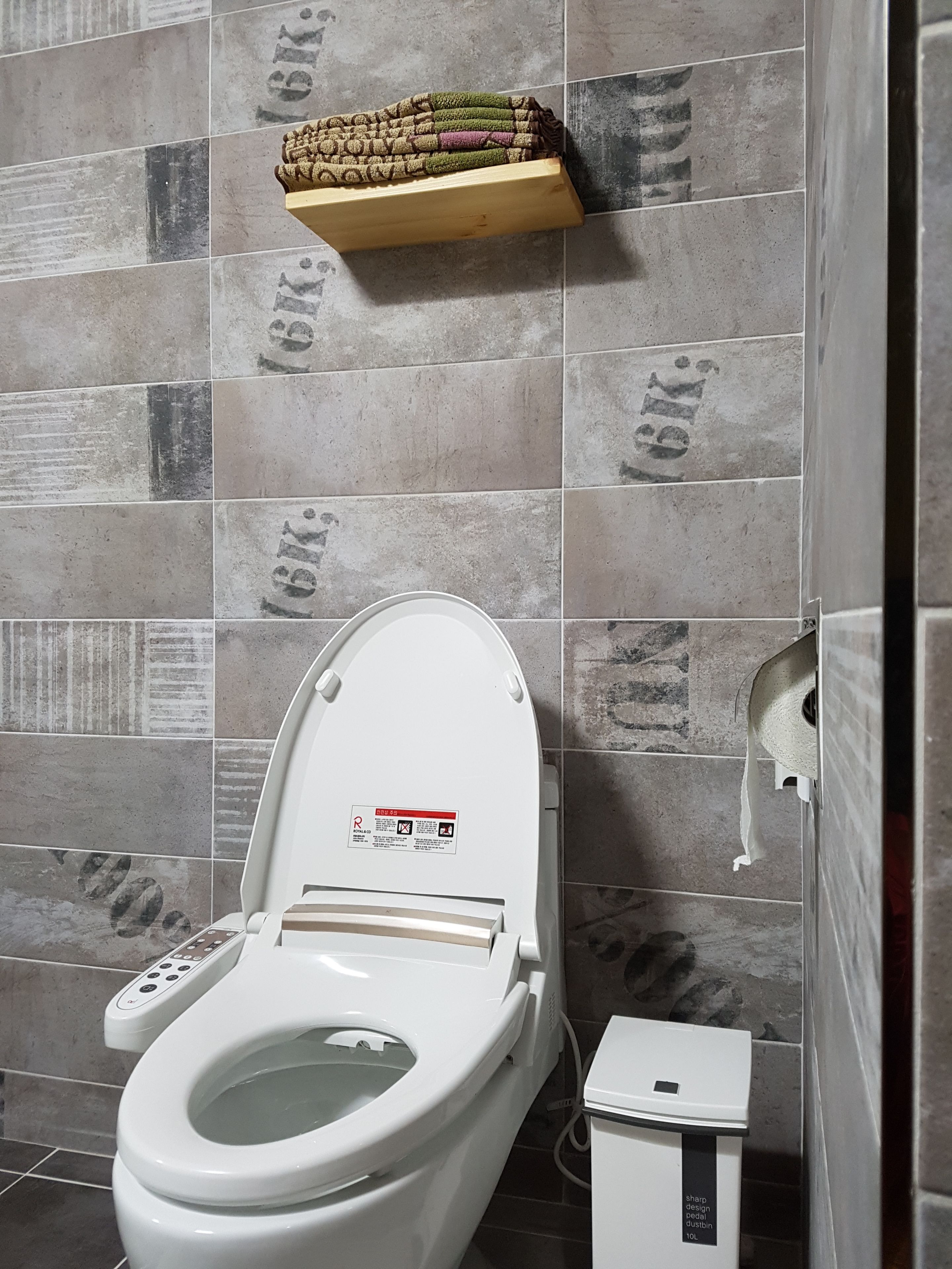 Un baño moderno con inodoro, secamanos y estante con toallas.