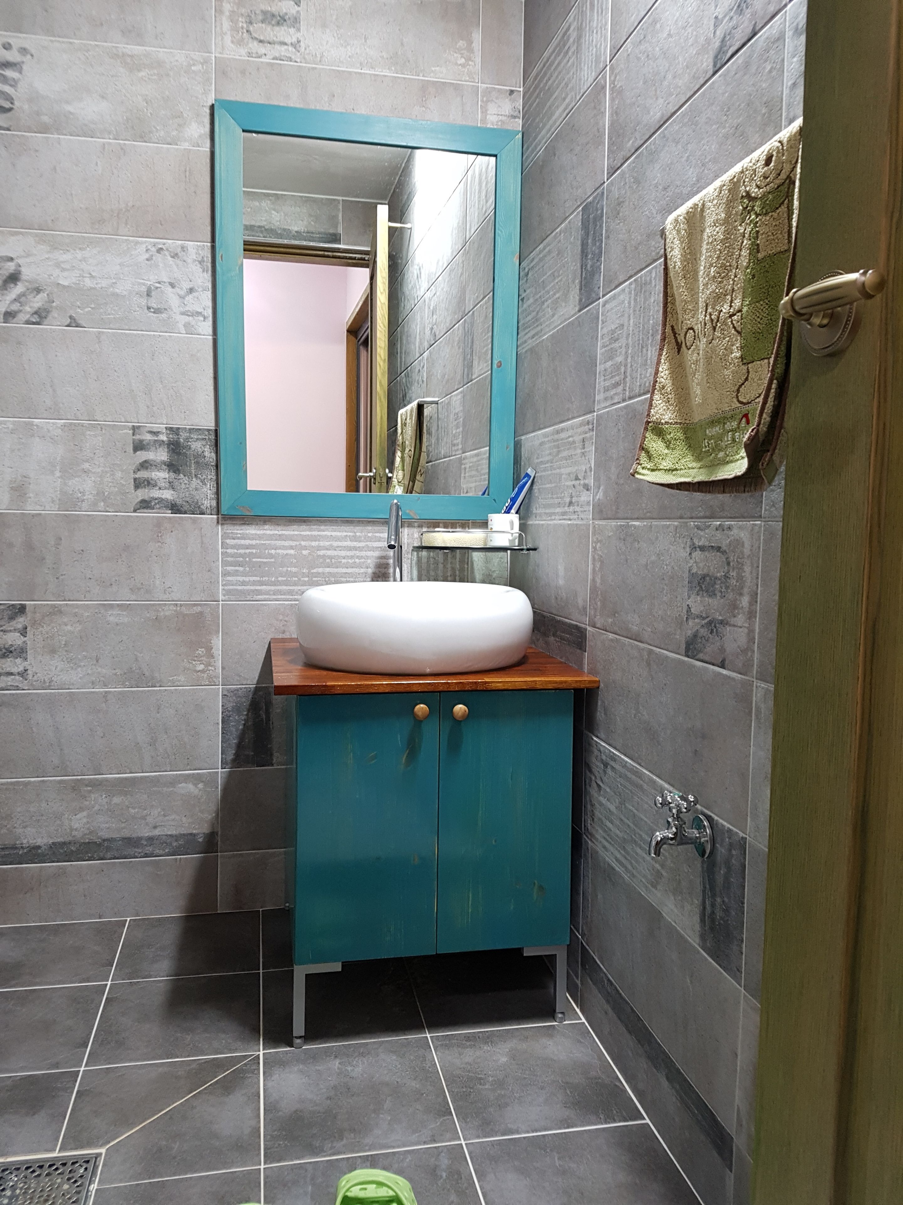 A bathroom with a white sink, teal cabinet, and a mirror with a teal frame.