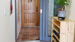 A wooden door with a small window, a potted plant, and a shoe rack with sandals. - dodo27 Guest House (Yeosu)