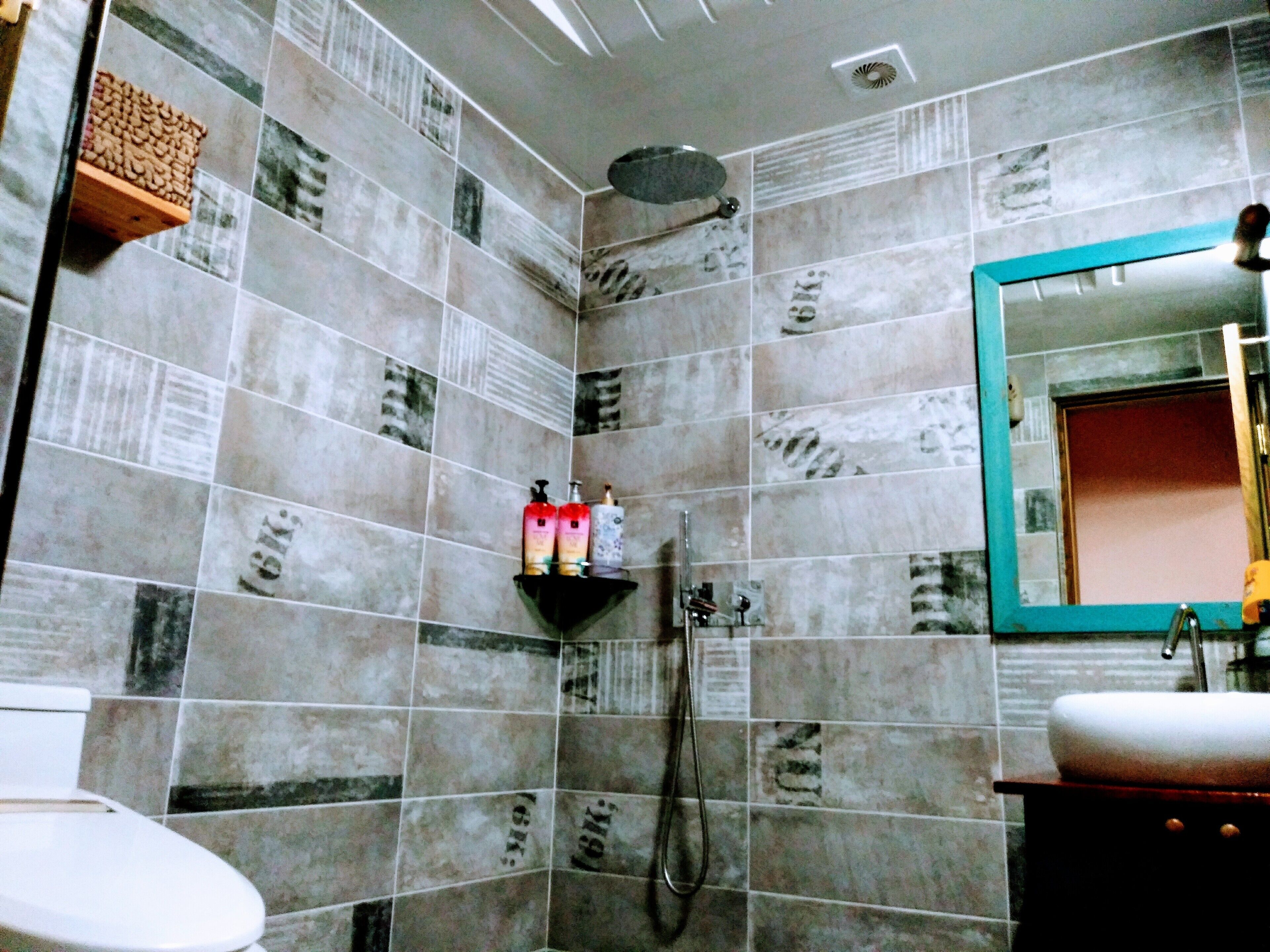 A bathroom with tiled walls, a shower, a sink, and a mirror.