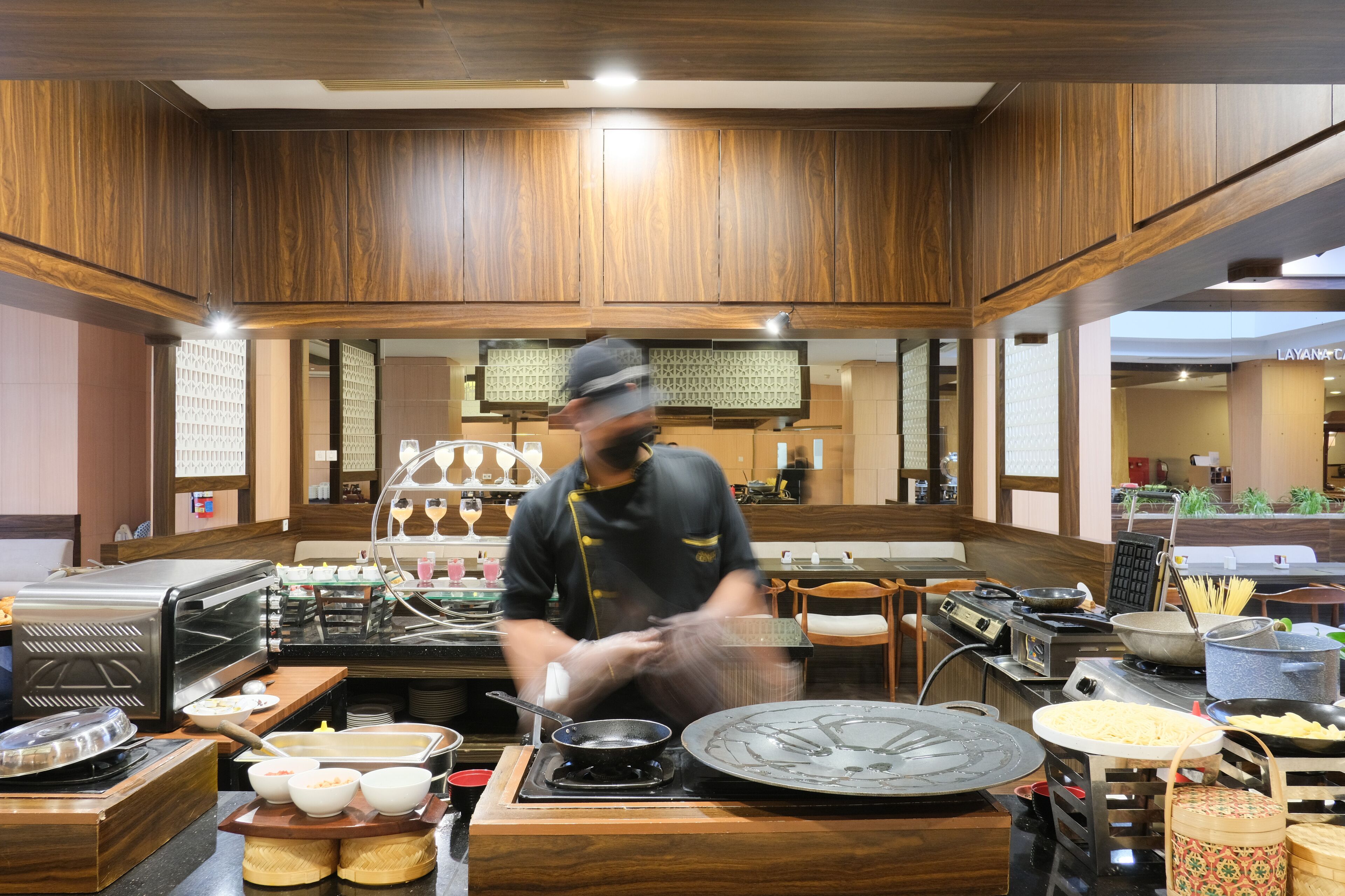 Montaje de bufé con varias estaciones de comida, incluyendo una parrilla caliente, una mesa de bufé y un mostrador con recipientes llenos de alimentos.