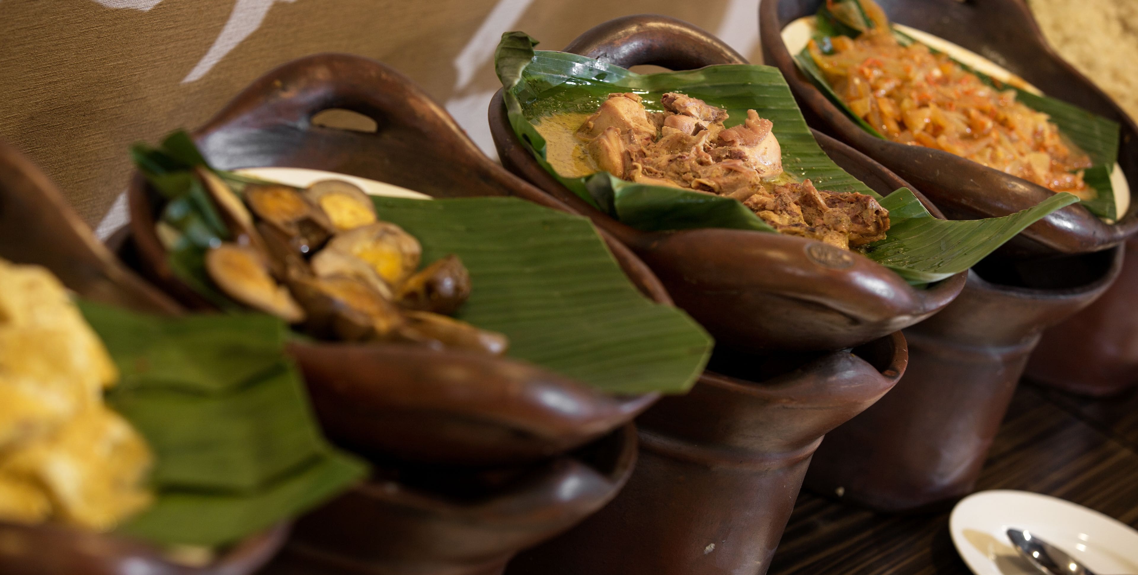 A table with several dishes served in traditional clay pots on banana leaves.