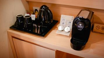 Una estación de café con cafetera, tazas y tetera sobre una encimera de madera.