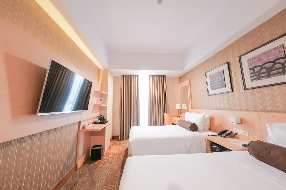 A hotel room with two beds, a TV mounted on the wall, a desk with a phone, and a small trash bin.