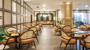 A restaurant with a long counter, wicker chairs, and a decorative wall with mirrors and plants. - Hotel Chanti (Semarang)