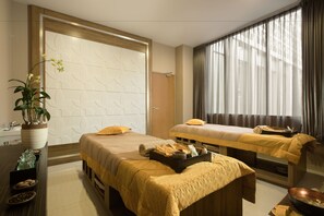 A hotel room with two beds, a large window with curtains, a potted plant, and a tray with towels and toiletries. - Hotel Chanti (Semarang)