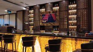 A bar area with a long counter, multiple bar stools, and a television mounted on the wall. - Hotel Chanti (Semarang)