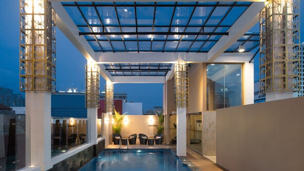 An indoor swimming pool with a glass ceiling, wooden deck, and seating area. - Hotel Chanti (Semarang)