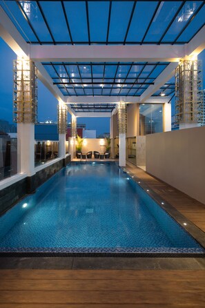 An indoor swimming pool with a glass ceiling, wooden deck, and seating area. - Hotel Chanti (Semarang)
