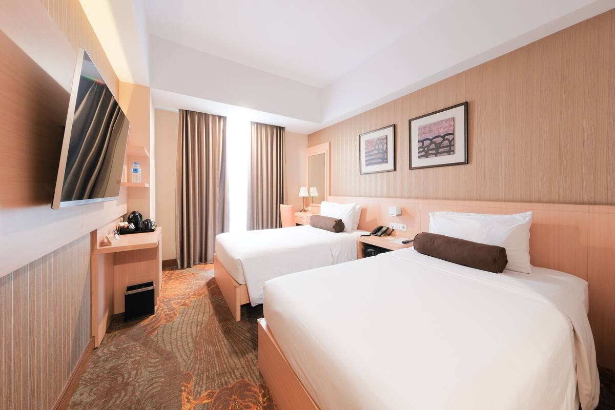 A hotel room with two beds, a flat-screen TV, a desk with a lamp, and a bathroom.