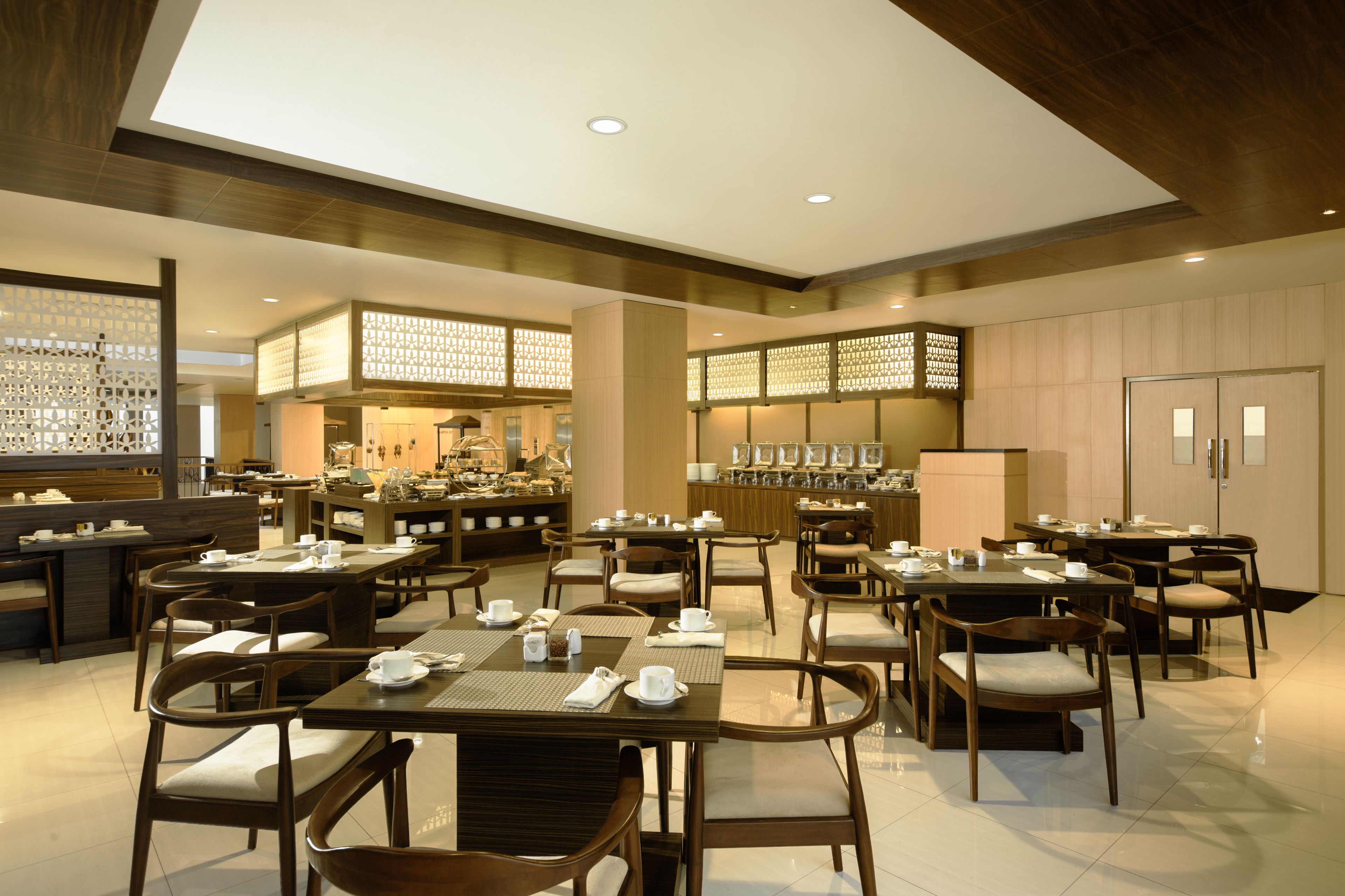 A spacious dining area with multiple tables and chairs, a kitchen in the background, and a modern interior design.