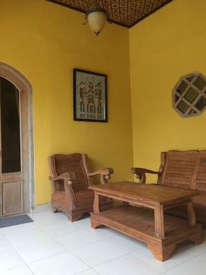A room with yellow walls, a wooden door, two wooden chairs, a wooden table, a framed picture, and a window with a wooden frame.