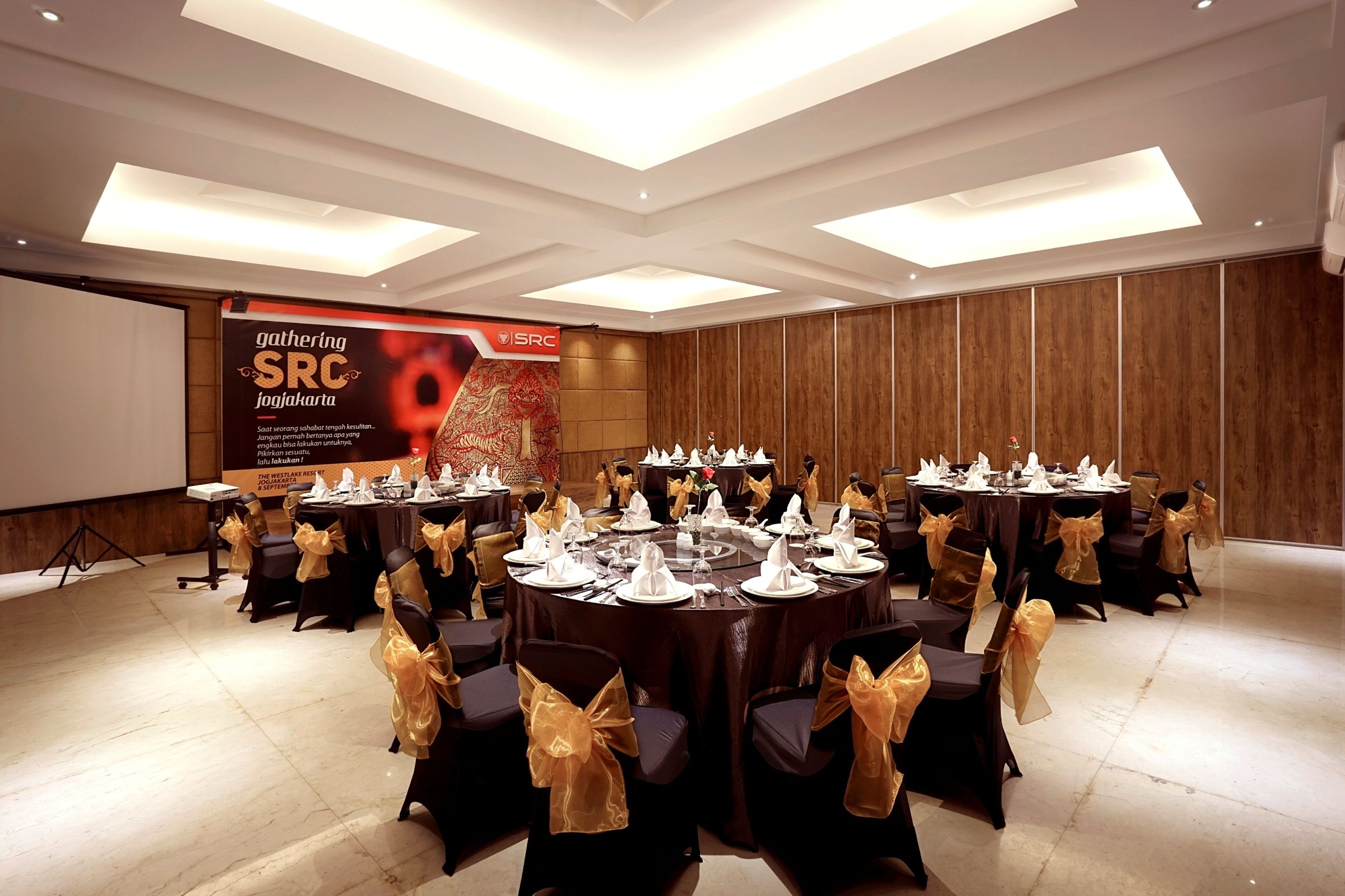 A conference room with round tables set for a meeting, each with a white tablecloth and gold sashes on the chairs.