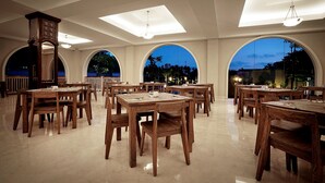 A spacious dining area with multiple wooden tables and chairs, large arched windows, and a high ceiling with skylights. - The Westlake Hotel & Resort Yogyakarta (Sleman)