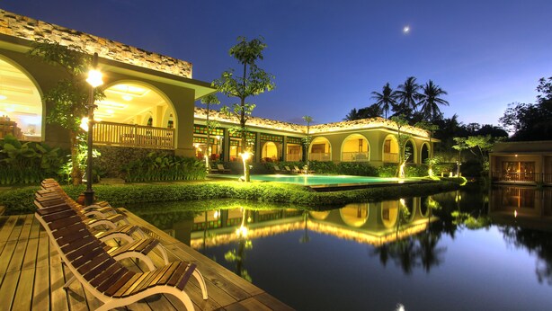 A tranquil hotel courtyard at dusk with a reflective pool, wooden deck, and illuminated architecture. - The Westlake Hotel & Resort Yogyakarta (Sleman)