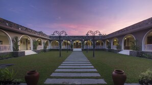 A courtyard with a central pathway leading to a building entrance, surrounded by arches and greenery. - The Westlake Hotel & Resort Yogyakarta (Sleman)